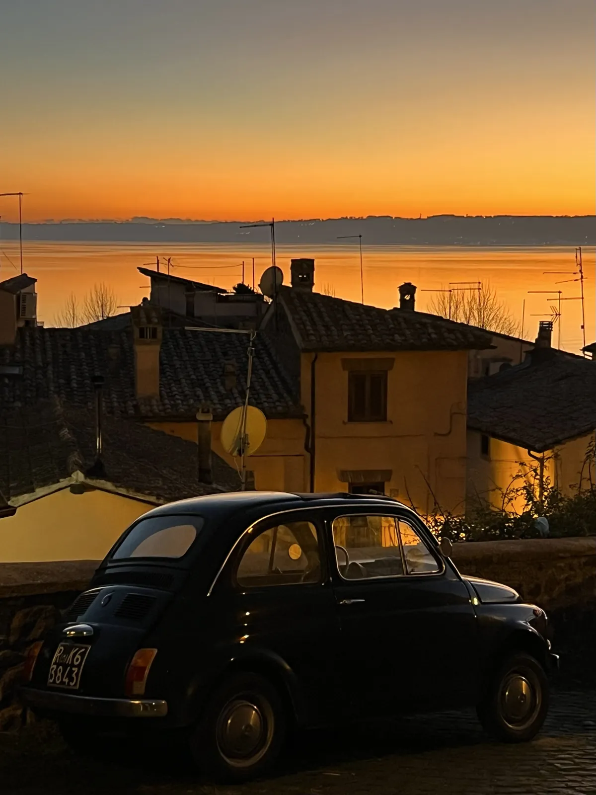 Vintage Fiat 500 over Trevignano rooftops at sunset